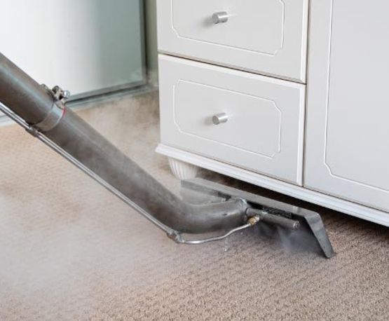 Professional carpet steam cleaning being performed near a wooden cabinet
