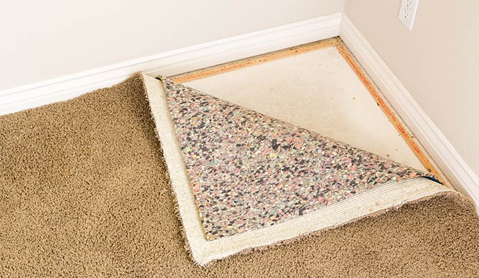 A view of a room corner with carpet pulled back to show the underlying padding and concrete subfloor