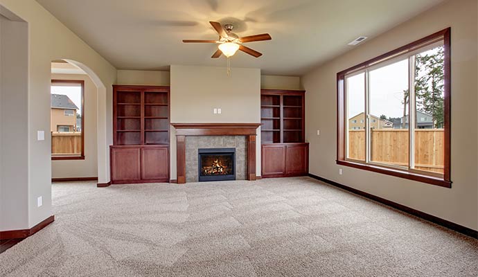 A spacious living room featuring freshly vacuumed tan carpet with visible lines, a fireplace, and built-in wooden bookshelves
