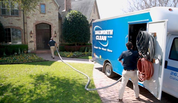 Technicians pulling a hose from a blue cleaning service van to a residential home