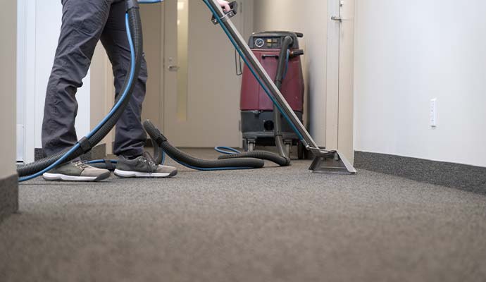 Technician using a wand to clean carpet in an office hallway
