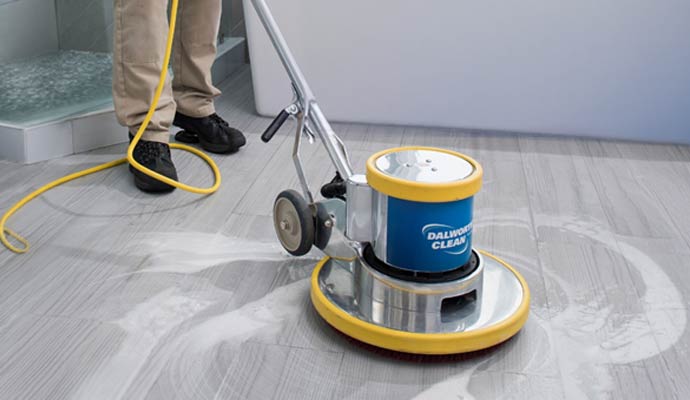 A technician using a professional Dalworth Clean floor buffer to polish and clean grey stone tile flooring