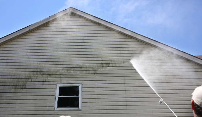 Professional worker pressure cleaning house wall