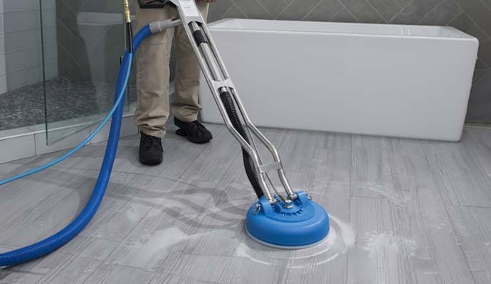 Technician cleaning bathroom tile floor with a rotary tool
