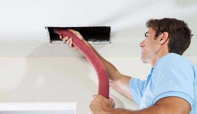 Technician using a vacuum hose to clean a ceiling air duct