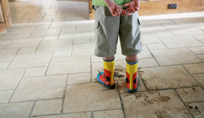 Kid is standing on the floor with a dirty rain shoe.